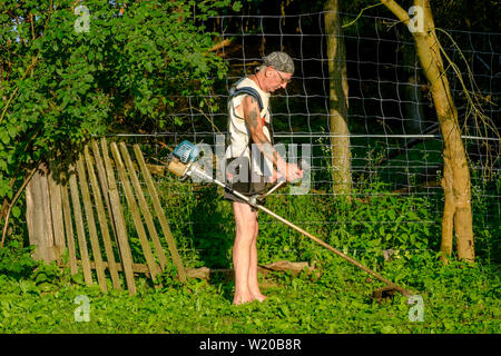 L'homme à l'aide d'un strimmer de couper l'herbe et les mauvaises herbes dans un jardin zala hongrie Banque D'Images