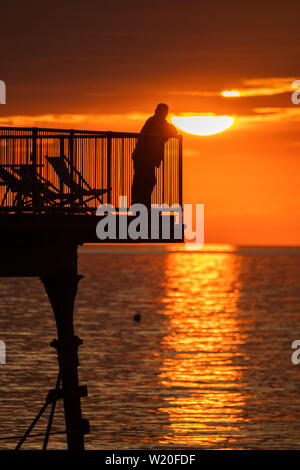 Pays de Galles Aberystwyth UK, jeudi 04 juillet 2019 Royaume-Uni : Météo personnes debout à la fin de la station balnéaire d'Aberystwyth tronqué pier sont silhouetté contre le ciel tout en regardant le coucher du soleil glorieux à Aberystwyth, sur la côte de la Baie de Cardigan, l'ouest du pays de Galles. Crédit photo : Keith Morris//Alamy Live News Banque D'Images