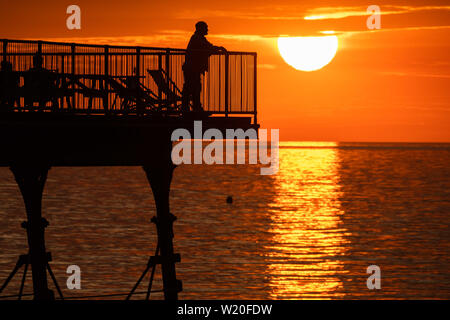 Pays de Galles Aberystwyth UK, jeudi 04 juillet 2019 Royaume-Uni : Météo personnes debout à la fin de la station balnéaire d'Aberystwyth tronqué pier sont silhouetté contre le ciel tout en regardant le coucher du soleil glorieux à Aberystwyth, sur la côte de la Baie de Cardigan, l'ouest du pays de Galles. Crédit photo : Keith Morris//Alamy Live News Banque D'Images