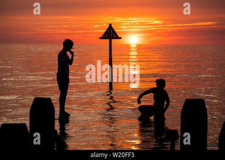 Pays de Galles Aberystwyth UK, jeudi 04 juillet 2019 Royaume-Uni Météo : un jeune couple est silhouetté contre le ciel comme ils l'équilibre sur la jetée en bois de la mer calme et de regarder le coucher du soleil glorieux à Aberystwyth, sur la côte de la Baie de Cardigan, l'ouest du pays de Galles. Crédit photo : Keith Morris//Alamy Live News Banque D'Images