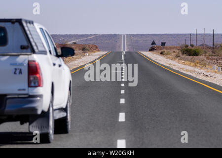 White Toyoya Hilux pick-up camion conduisant le long d'une très droit et long la route goudronnée à travers le désert du Kalahari, en Namibie Banque D'Images