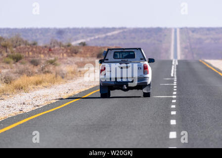 White Toyoya Hilux pick-up camion conduisant le long d'une très droit et long la route goudronnée à travers le désert du Kalahari, en Namibie Banque D'Images