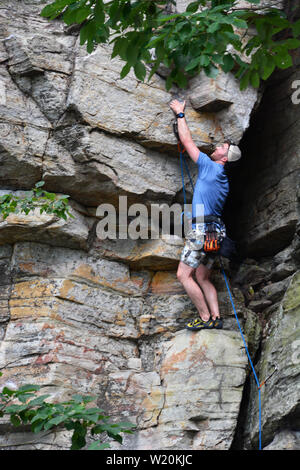 Un jeune grimpeur travaille son chemin d'une falaise sur le rebord du sentier du printemps à Pilot Mountain State Park en Caroline du Nord. Banque D'Images