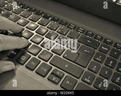 Un clavier d'ordinateur portable allumé, sur le côté gauche, vous pouvez voir trois doigts en appuyant sur les boutons. Un détail dans une image en noir et blanc. Fermer Banque D'Images