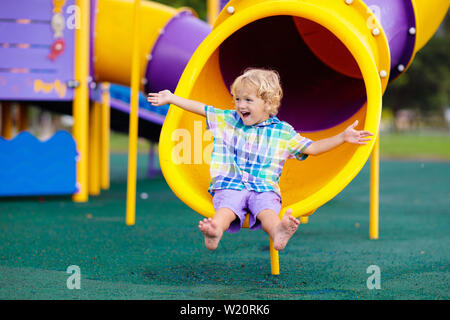 Enfant jouant sur l'aire de jeux extérieure. Les enfants jouent sur l'école ou l'école maternelle cour. Kid active sur diapositive colorées et swing. Activité d'été sain pour chi Banque D'Images