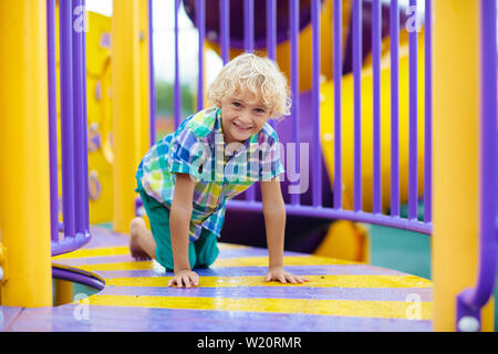 Enfant jouant sur l'aire de jeux extérieure. Les enfants jouent sur l'école ou l'école maternelle cour. Kid active sur diapositive colorées et swing. Activité d'été sain pour chi Banque D'Images