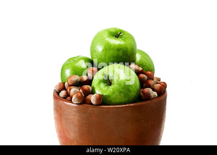 Une faïence marron vert bol rempli de pommes Granny Smith et Brown noisettes isolé sur fond blanc. Banque D'Images