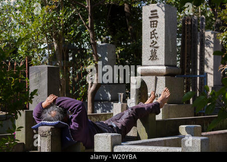 Un homme sans abri dort sur des pierres tombales dans un cimetière à Azabu, Tokyo, Japon. Banque D'Images