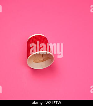 Tasse rouge en papier avec les bords ondulés par le café à l'envers sur un fond rose Banque D'Images