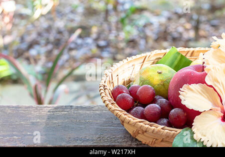 Pomme, orange et raisin à tisser des paniers en bambou avec décorations florales arbres flous d'arrière-plan. Banque D'Images