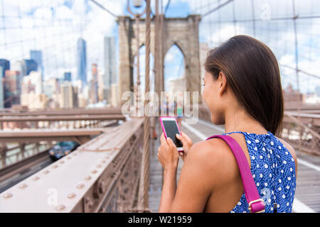 Sms Smartphone fille sur le pont de Brooklyn en milieu urbain La ville de New York, Manhattan USA. Vue depuis l'arrière de méconnaissable business woman holding phone la lecture ou l'utilisation des médias sociaux en été. Banque D'Images