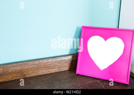 Cadre photo coeur rose sur la table en bois avec fond mur bleu, l'espace pour le texte Banque D'Images