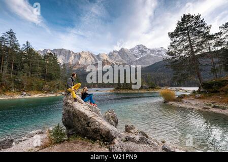 Deux randonneurs assis sur un rocher sur le rivage, vue dans la distance, lac Eibsee devant avec Zugspitzmassiv, Zugspitze Wetterstein, près de la plage Banque D'Images