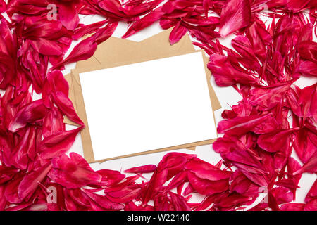 Le papier blanc et de l'enveloppe rouge avec pétales de pivoines sur fond gris Banque D'Images
