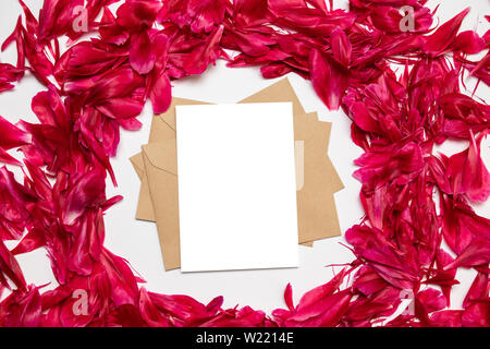 Le papier blanc et de l'enveloppe rouge avec pétales de pivoines sur fond gris Banque D'Images