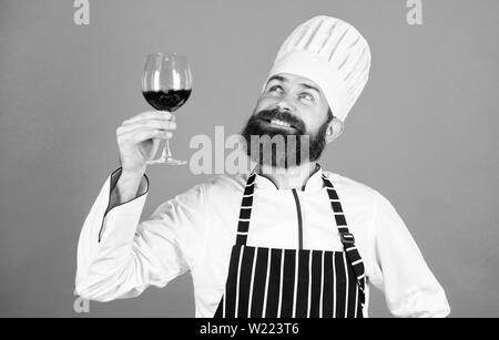 Je recommande ce vin. Confiant homme sommelier examinant avec verre de vin. Ce vin est tout simplement parfait. Heureux homme barbu. Chef professionnel en uniforme cook. Boisson alcoolisée. Vin rouge dans le verre. Banque D'Images