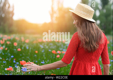 Belle jeune femme romantique au pied du chapeau de paille de pavot sur champ de fleur et prend coquelicots. Couleurs d'été doux coucher du soleil Banque D'Images