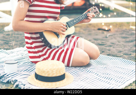 Close-up of a Girl holding a ukulele, assis sur une couverture, Garland orne l'arrière-plan, l'atmosphère de la maison de vacances en plein air et de la convivialité. Mu Banque D'Images