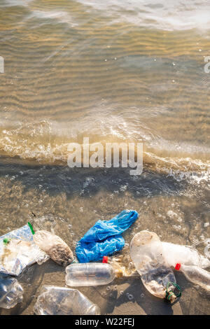 Le sac en plastique et les bouteilles sur la plage, mer et la pollution de l'eau concept. Corbeille vide (emballage alimentaire) jetés à la mer, vue du dessus avec des vagues Banque D'Images