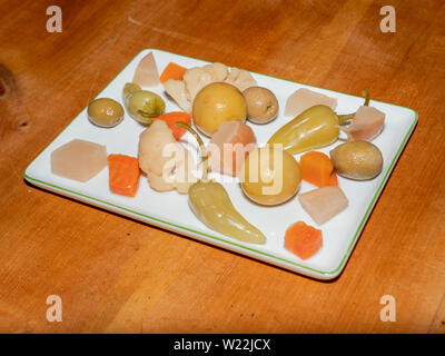 Un assortiment de cornichons turc Épicé - appelé Tursu - citron, poivre, olives, carottes sur une plaque rectangulaire blanche sur une table en bois Banque D'Images