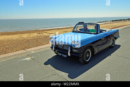 Classique Bleu Triumph Herald voiture décapotable roulant le long de la promenade. Banque D'Images