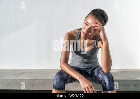 Remise en forme fatigué femme exécutant la transpiration en faisant une pause d'entraînement cardio difficile la formation. Épuisé runner assis avec maux de sentiment d'épuisement et de déshydratation, à partir de l'élaboration à la salle de sport en plein air. Banque D'Images