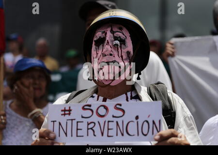 Caracas, Venezuela. 05 juillet, 2019. 'SOS - Intervention", est écrit sur l'affiche d'un manifestant masqué lors d'un rassemblement contre le gouvernement du chef de l'Etat Maduro. Le chef de l'opposition et l'auto-nommé président par intérim Guaido avait appelé à des manifestations contre le gouvernement le 5 juillet, jour de l'indépendance du Venezuela. Credit : Rafael Hernandez/dpa/Alamy Live News Banque D'Images