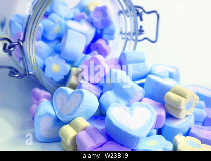 Bleu pastel et de couleur violette et coeur en forme de fleurs bonbons guimauve de pot de verre éparpillés sur le tableau blanc Banque D'Images