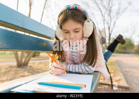 Peu d'artiste belle dessin avec crayons de couleur, fille assise sur un banc de parc ensoleillée d'automne, l'heure d'or Banque D'Images