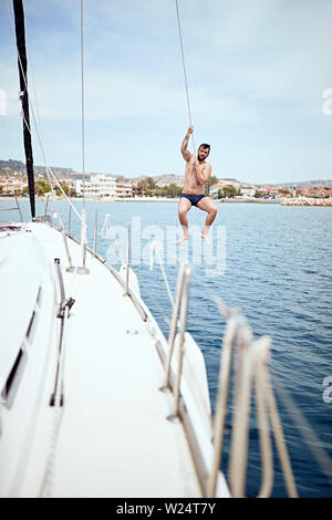 Heureux jeune homme sauter de bateau à voile en mer. Banque D'Images