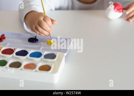 Les mains de l'enfant peint des oeufs de Pâques, les peintures et les pinceaux sur tableau blanc. Préparation de la Pâques. Mains pour enfants dessiner avec des couleurs. Banque D'Images