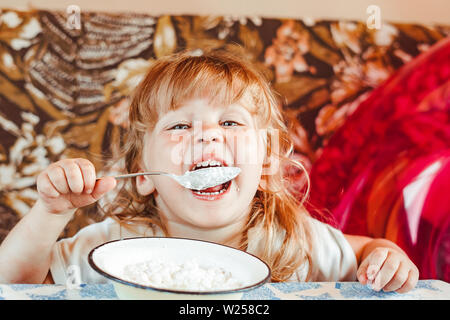 Happy little girl eating une cuillerée de fromage blanc alors qu'il était assis à la table Banque D'Images