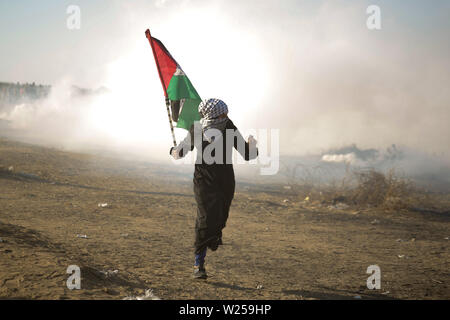 Gaza, la Palestine. 05 juillet, 2019. Manifestant palestinien portant un drapeau, s'enfuit de la fumée des gaz lacrymogènes qu'ils ont été soumis à au cours d'une manifestation appelant à la fin de l'blocus israélien de Gaza et de la demande pour le droit de rentrer chez eux à la frontière entre Israël et Gaza, dans le sud de la bande de Gaza. Credit : SOPA/Alamy Images Limited Live News Banque D'Images