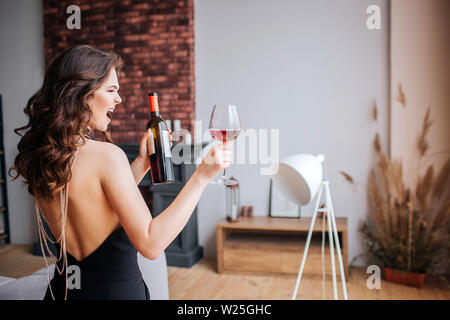 Jeune femme a des problèmes avec l'alcool. Beau bien construit et modèle slim en costume noir tenir la bouteille et le verre à vin. Retour permanent et crier. Banque D'Images