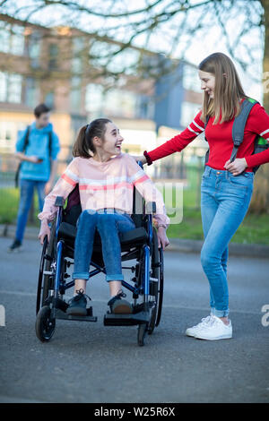 Teenage Girl In Wheelchair Talking With Friend comme ils quittent l'école secondaire Banque D'Images