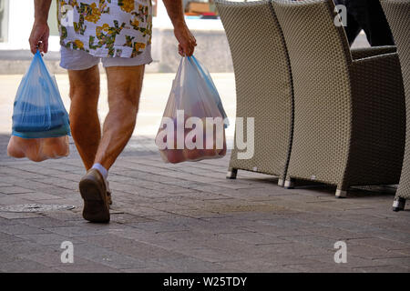La moitié inférieure de l'homme non identifié la marche loin avec des fruits et légumes dans plusieurs sacs en plastique Banque D'Images
