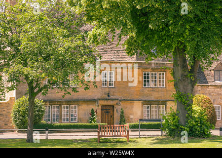 Cotswold cottage en pierre traditionnelle géorgienne baigné de lumière d'été donnant sur la place du village d''un coin salon avec un banc Banque D'Images