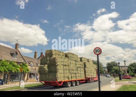 Un agriculteur le transport d'une des balles de foin sur un plein camion à travers le magnifique village des Cotswolds de Broadway dans le Worcestershire. Banque D'Images