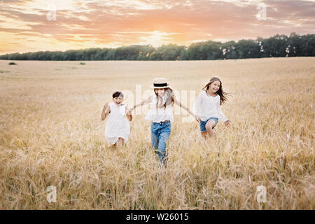 Groupe de trois filles souriant s'exécutant dans le champ de blé au coucher du soleil Banque D'Images