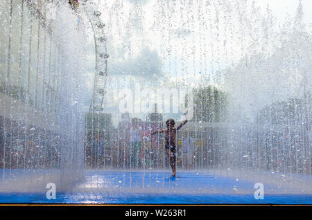 Un jeune garçon profitant de la météo de l'été à l'intérieur d'une fontaine de la rue de Londres, Angleterre Banque D'Images