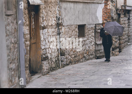 Ohrid, Macédoine du Nord - Avril 2019 : Femme avec parapluie marche sur une rue étroite dans la ville d'Ohrid Banque D'Images