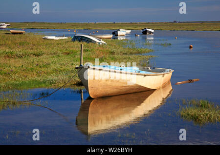 Un canot et de réflexion avec d'autres bateaux amarrés par des marais salés de la côte nord du comté de Norfolk à Blakeney, Norfolk, Angleterre, Royaume-Uni, Europe. Banque D'Images