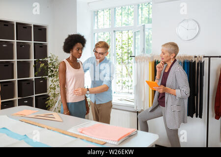 Prendre des mesures correctes. Adapter la mesure d'une joyeuse belle jeune femme sérieuse à la recherche d'un female fashion designer Banque D'Images