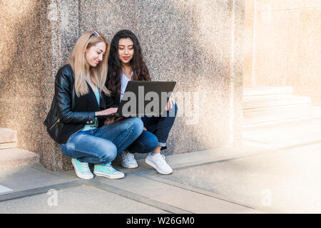 Deux belles les étudiants de différents pays sont assis sur le mur face à un ordinateur portable ouvert Banque D'Images