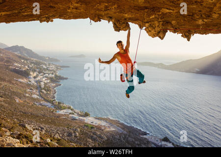 Male rock climber hanging sur falaise avec une main et showing thumb up Banque D'Images