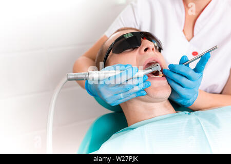 Une femme dentiste examine la cavité buccale du patient avec un outil avec un miroir. Portrait en gros plan d'un patient avec une bouche ouverte, un médecin à Banque D'Images