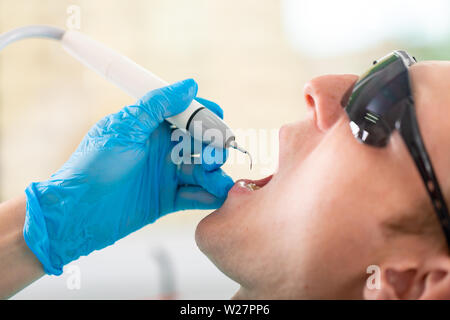 Une femme dentiste examine la cavité buccale du patient avec un outil avec un miroir. Portrait en gros plan d'un patient avec une bouche ouverte, un médecin à Banque D'Images