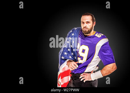 American football player closeup portrait. Joueur de football américain avec un drapeau américain dans ses mains. Notion de patriotisme, célébration. Banque D'Images