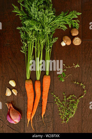 Frais de la ferme des carottes crues avec tops avec champignons crimini, gousses d'ail, les échalotes, l'origan et branches de thym sur fond de bois rustique foncé f Banque D'Images