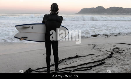 Un surfeur de St James sur Danger Beach envisage de retourner dans la mer tout en regardant une autre série de vagues sur la péninsule du Cap, Afrique du Sud Banque D'Images